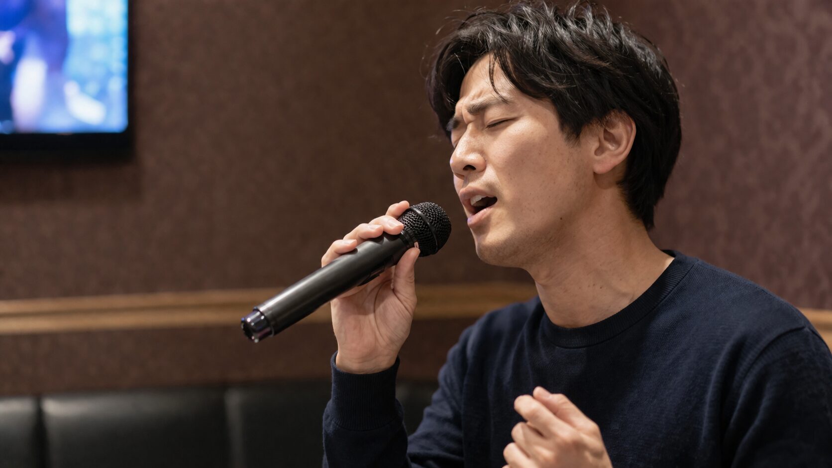 サビで裏声への切り替えに挑む男性がマイクを握る場面